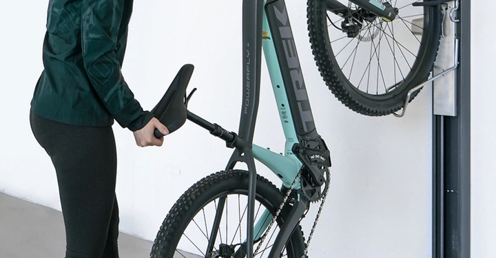 Frau hebt Fahrrad auf vertikalen Wandhalter in einem Raum