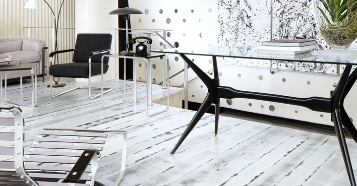 Galerie-Bild 9: Ein schwarzer Stuhl steht auf einem weiß gestrichenen Holzboden neben einem Glastisch, auf dem Bücher und eine Pflanze liegen, in einem modern eingerichteten Raum mit Punktmuster an der Wand.