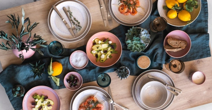 Mediterran gedeckter Holztisch mit der Villeroy & Boch Kollektion Perlemor in den Farben Coral und Sand, dekoriert mit Meeresfrüchten, Zitronen und Sukkulenten.