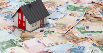 Ein kleines Modellhaus steht auf einem Haufen von Eurobanknoten in verschiedenen Werten und Farben.