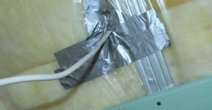 Galerie-Bild 13: Ein weißes Kabel wird mit silbernem Klebeband an einer Metallstange befestigt, die von gelber Isolierung und Plastikfolie umgeben ist.