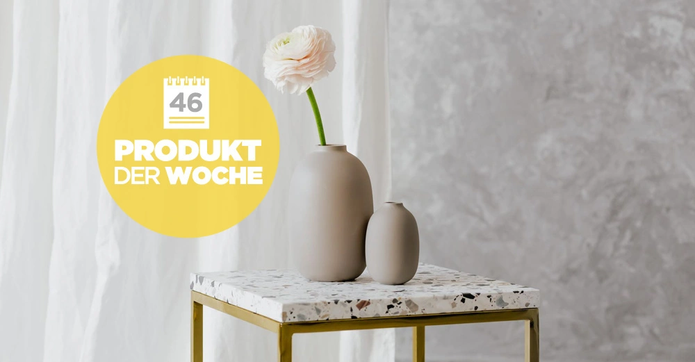 Zwei beige Vasen stehen auf einem Tisch aus Terrazzo mit goldenen Beinen Blaue Blume aus einer Vase weißer Vorhang links graue Wand rechts Text auf gelbem Kreis 46 PRODUKT DER WOCHE