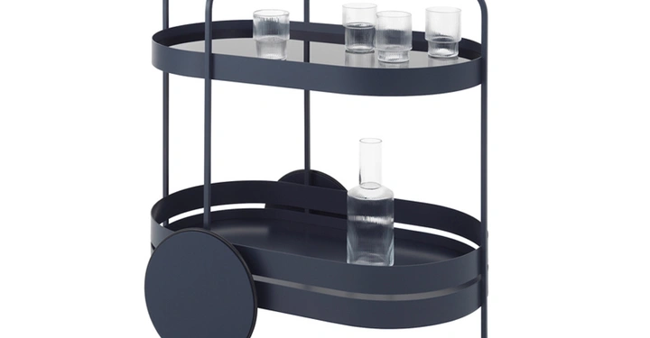 Dunkelblauer Servierwagen trägt auf zwei Etagen mehrere Gläser und eine Karaffe. Er steht in einem einfachen weißen Raum.