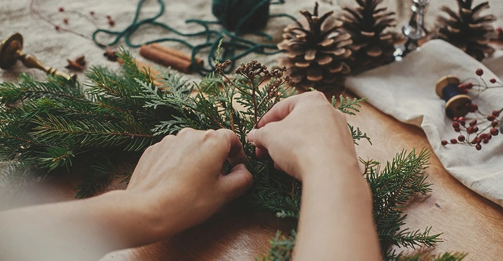 Hände beim Binden eines traditionellen Adventskranzes aus Tannenzweigen, ein Brauch, der auf den Theologen Johann Hinrich Wichern zurückgeht.