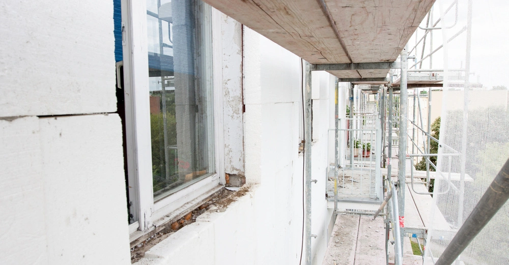 Fensterrahmen ohne Glas und Dämmplatten an der Außenwand eines Gebäudes Gerüststruktur umgibt das Gebäude und zeigt, dass es sich auf einer Baustelle befindet.