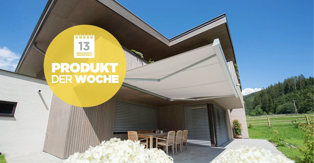 Ein modernes Haus mit einer großen ausziehbaren Markise die über eine Terrasse mit Tisch und Stühlen gespannt ist im Hintergrund grüne Hügel und Bäume. Text: 13 PRODUKT DER WOCHE