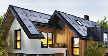 Großes Einfamilienhaus in Abenddämmerung, von innen beleuchtet mit großen Photovoltaik-Paneelen am Dach. Im Vordergrund Sträucher und Bäume.