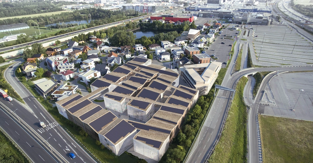 Luftaufnahme eines Stadtgebiets mit modernen Gebäuden und Solarmodulen auf den Dächern linke Straßenseite mit Autos und umliegenden Grünflächen im Hintergrund Industriegebiet und Parkplätze.