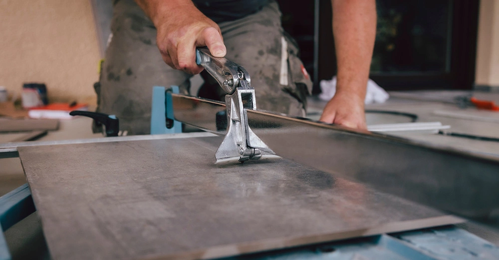 Professionelles Fliesenschneiden mit manuellem Fliesenschneider. Handwerker bei der Bearbeitung von Feinsteinzeug auf Baustelle.