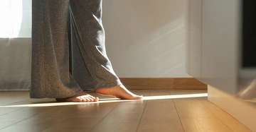 Eine Person geht barfuß auf einem warmen Parkettboden und genießt den Komfort einer Fußbodenheizung. Die unsichtbare Heizlösung sorgt für angenehm warme Füße und ein behagliches Raumklima.