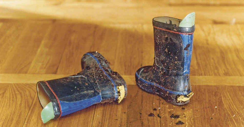 Ein Paar dreckiger Kindergummistiefel auf Holzparkett.