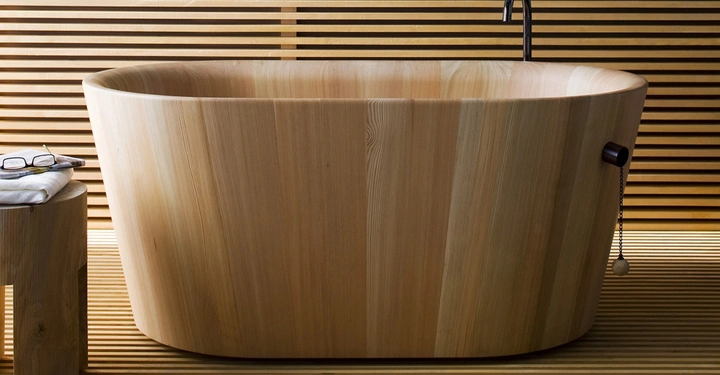 Galerie-Bild 4: Holzbadewanne steht still in einem modernen, minimalistischen Badezimmer. Daneben befindet sich ein kleiner Holzhocker mit einer Brille und einem Handtuch. Hintergrund aus horizontalen Holzplanken.