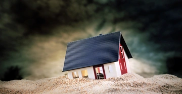 Nahaufnahme eines kleinen Modellhauses, das im Sand versinkt.