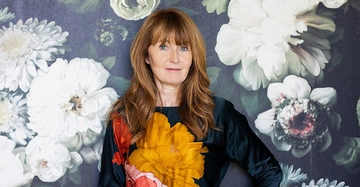 Frau steht selbstbewusst mit Blumenmuster an der Wand im Hintergrund Blumenmuster in verschiedenen Weißtönen und grünen Blättern