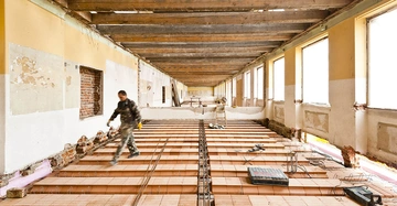 Ziegelfertigdecke in Altbau, Arbeiter geht über die fertige Decke, Fensterfront mit viel Tageslichteinfall, Werkzeuge auf der Decke zu sehen