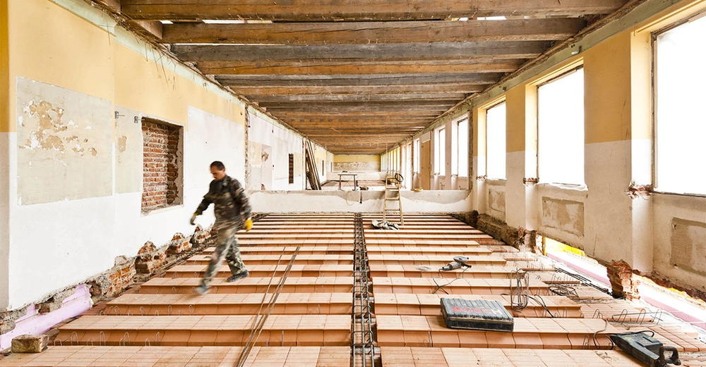 Ziegelfertigdecke in Altbau, Arbeiter geht über die fertige Decke, Fensterfront mit viel Tageslichteinfall, Werkzeuge auf der Decke zu sehen