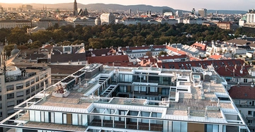 Moderne Gebäude mit Glasfassade Blick auf Stadt mit roten Dächern und bewaldetem Park im Hintergrund Skyline mit Kirchturm und Bergen in der Ferne Himmel leicht bewölkt
