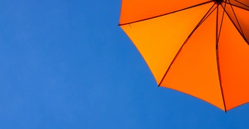 Knalloranger Sonnenschirm von unten fotografiert vor tiefblauem, wolkenlosem Himmel.