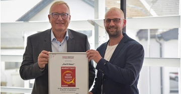 zwei Männer in Anzug und mit Brille halten stolz eine Auszeichnung in die Kamera