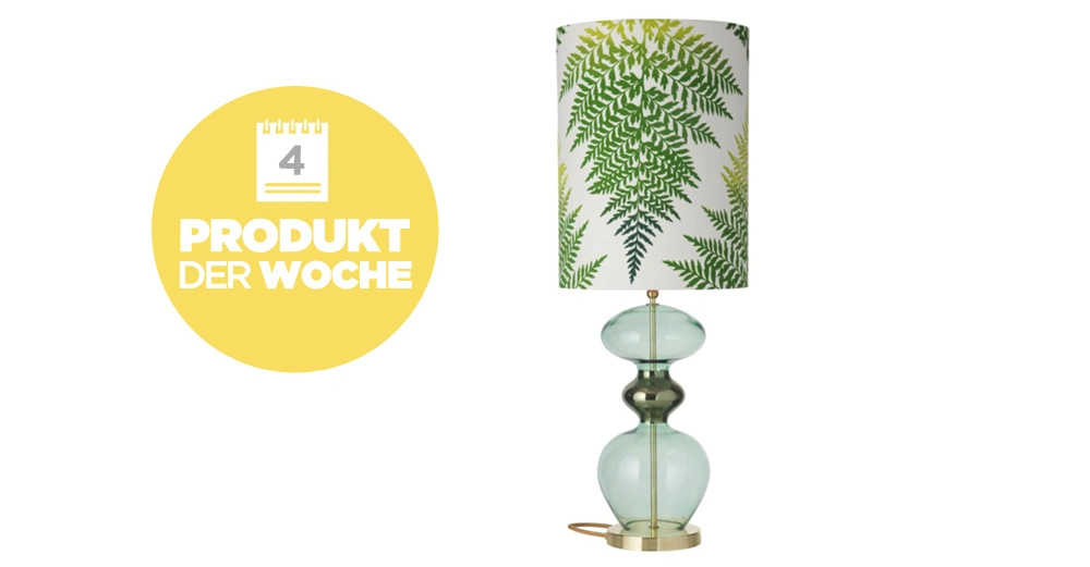 Eine Lampe steht auf einer Oberfläche. Der Schirm hat ein Farnblatt-Muster in Grün. Ein gelber Kreis daneben hat den Text: "4 PRODUKT DER WOCHE".