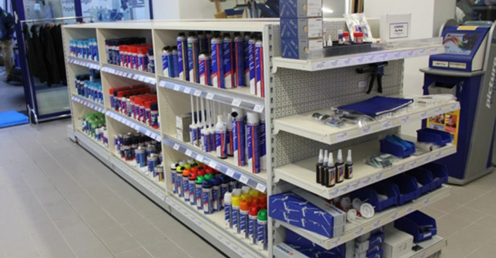 Galerie-Bild 6: Regal voll mit Baumaterialien steht in einem Geschäft links Klebstoffe und Silikone rechts Kleinteile und Werkzeuge Boden gefliest im Hintergrund Glaswand und ein Automat