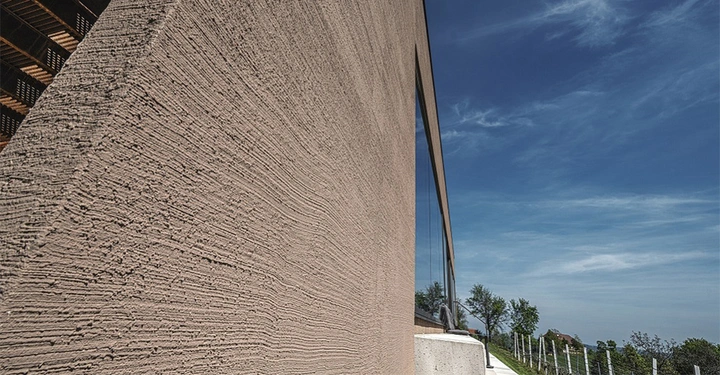 Galerie-Bild 3: Raue Wand eines modernen Gebäudes reflektiert Sonnenlicht an einem sonnigen Tag, Umgebung eines leicht bewölkten blauen Himmels und angrenzender Vegetation.