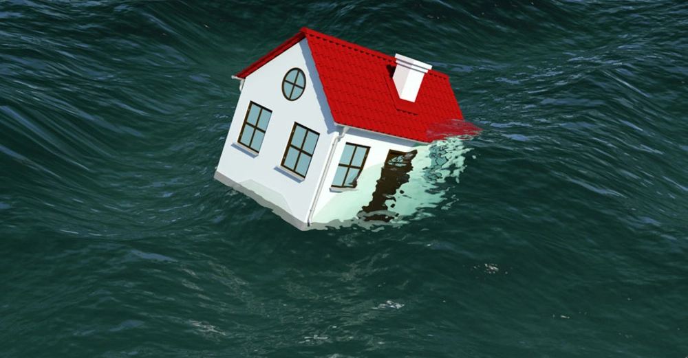 Ein weißes Haus mit rotem Dach schwimmt teilweise untergetaucht im offenen, welligen Meer.