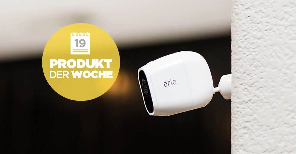Eine weiße Kamera ist an einer Wand montiert in einem Innenraum. Text im Bild: 19 PRODUKT DER WOCHE.