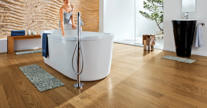 Galerie-Bild 2: Eine Frau in einem Handtuch füllt eine freistehende Badewanne in einem modernen Bad mit Holzfußboden und Steinwand. Ein Waschbecken und Dekorationen befinden sich in der Umgebung.