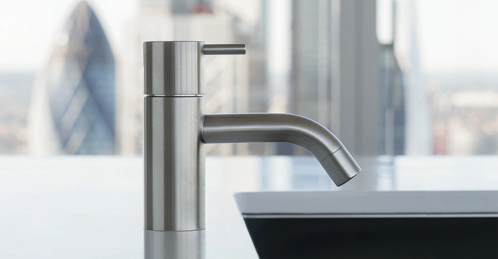 Ein Edelstahl-Wasserhahn steht still neben einem Waschbecken mit einer modernen Stadtlandschaft und Hochhäusern im Hintergrund.