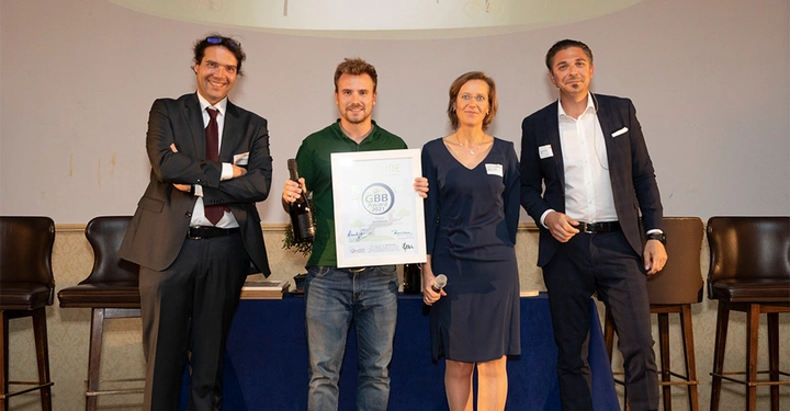 Galerie-Bild 8: Vier Personen stehen lächelnd vor einem Podium, eine Person hält eine Urkunde mit der Aufschrift Urkunde GBB Award 2021, zwei Personen sind in Businesskleidung und eine in Jeans und T-Shirt.