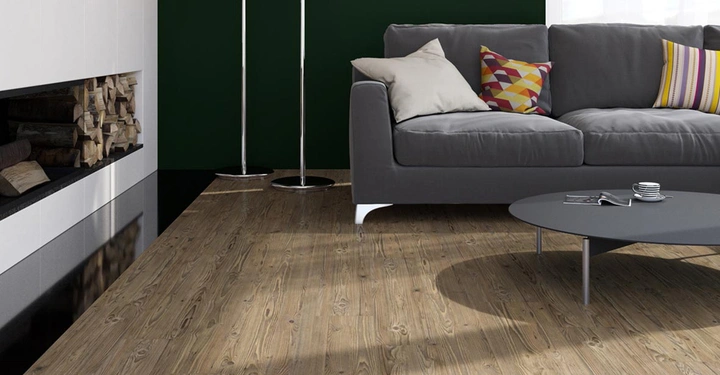 Graues Sofa mit bunten Kissen steht neben zwei Stehlampen und einem niedrigen runden Couchtisch in einem modernen Wohnzimmer mit Holzboden und dunkelgrüner Wandfarbe neben einem Kamin mit gestapeltem Brennholz.