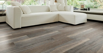 Ein weißes Ecksofa steht in einem modern eingerichteten Wohnzimmer vor großen Fenstern mit Blick auf einen grünen Garten Holzboden und ein paar Kissen auf dem Sofa.