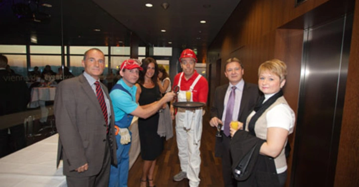 Galerie-Bild 57: Sechs Personen posieren lächelnd zusammen in einem Veranstaltungsraum zwei tragen Bauarbeiterbekleidung und Helme der Raum hat Holzböden und moderne Wände im Hintergrund stehen ein Tisch und Fenster textfrei