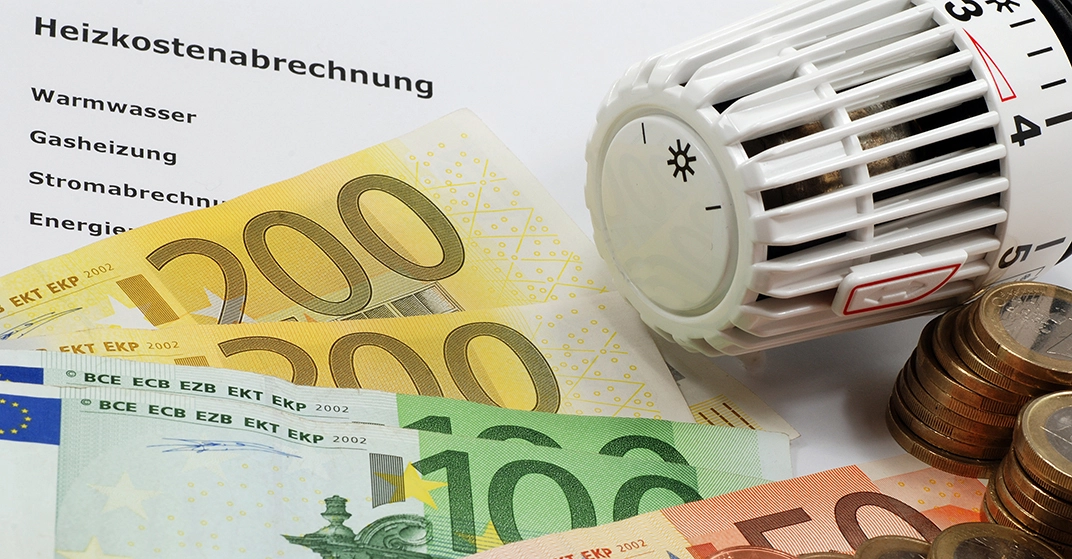 Eine Heizkostenabrechnung mit mehreren Hundert-Euro-Scheinen und Münzen, sowie einem Heizungsregler.