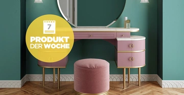 Rosa Schminktisch und Hocker in einem Raum mit grünen Wänden und Parkettboden. Ein runder Spiegel ist an der Wand angebracht. Text: 7 PRODUKT DER WOCHE.