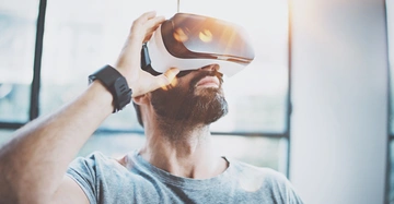 Mann benutzt Virtual-Reality-Headset in einem hellen Raum mit großen Fenstern im Hintergrund.