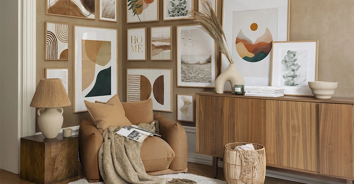 Sessel mit Decke und Buch stehend vor einer mit Kunstwerken dekorierten Wand im Wohnzimmer vor einer modernen Holzkommode; umgeben von Vasen, Lampe und Dekor. Text HOME auf einem Bild.