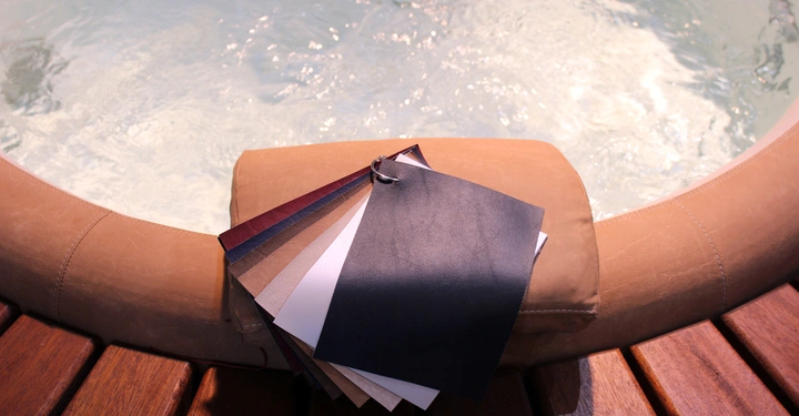 Galerie-Bild 26: Ein Musterbuch mit verschiedenen Lederproben liegt auf einem braunen Polster am Rand eines Whirlpools mit sprudelndem Wasser in einer Umgebung aus Holzpaneelen.