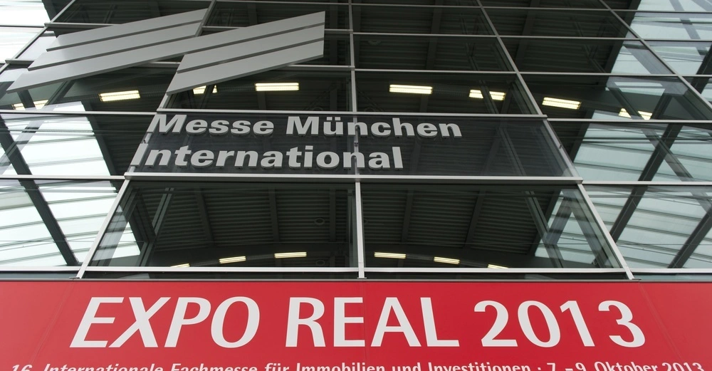 Gebäude mit Glasfassade zeigt großes Logo Messe München International und darunter ein rotes Banner mit weißer Schrift EXPO REAL 2013 16. Internationale Fachmesse für Immobilien und Investitionen 7.-9. Oktober 2013