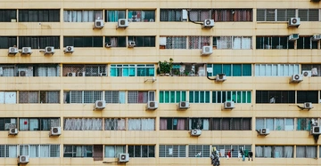 Mehrstöckiges Gebäude mit gelber Fassade und zahlreichen Fenstern Klimaanlagen an fast jedem Fenster Waschleinen mit Kleidung Sichtbar Wohnungen mit unterschiedlichen Vorhängen Stadtumgebung