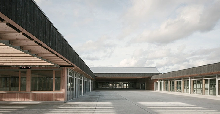 Innenhof eines einstöckigen Gebäudes aus Holz mit großer Glasfassade, gepflasterter Boden, Sonneneinstrahlung