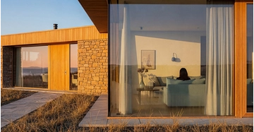 Außenaufnahme eines modernen Bungalows, Blick durch Glasfront in das Wohnzimmer