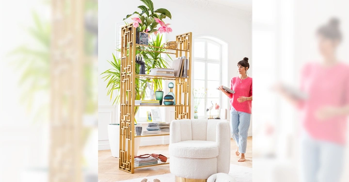 Galerie-Bild 7: Ein Bücherregal steht neben einem hellen Sessel In einem Wohnzimmer neben einem großen Fenster liegt ein Hund auf einem Teppich Eine stehende Person im Hintergrund betrachtet ein Buch.