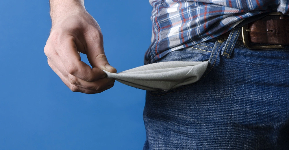 Hand zieht eine leere Hosentasche heraus Mann trägt karierte Hemd und Jeans blauer Hintergrund