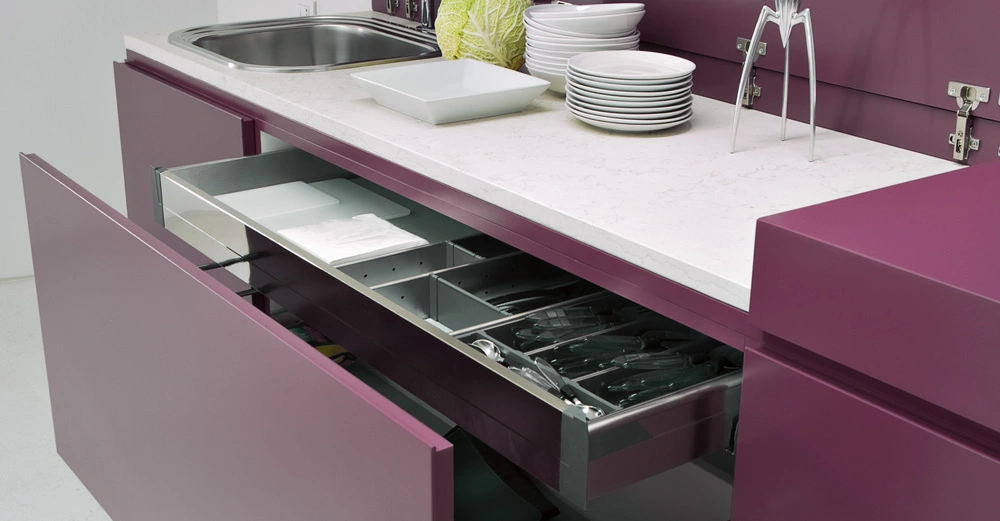 Offene Schublade mit Küchenutensilien Arbeitsfläche mit Gemüse und Geschirr sowie lila Küchenzeilen in einem modernen Küchenraum