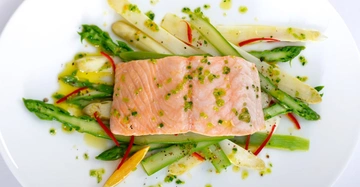 Frischer gedünsteter Lachs auf einem Bett aus dampfgegartem Gemüse. Sehr appetitlich auf Teller angerichtet.