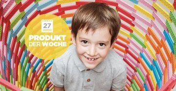 Ein lächelnder Junge, der ein graues Hemd trägt, kniet in einem bunt gewebten Korb. Der Hintergrund zeigt einen gelben Kreis mit Kalender-Icon und Text: 27 PRODUKT DER WOCHE.