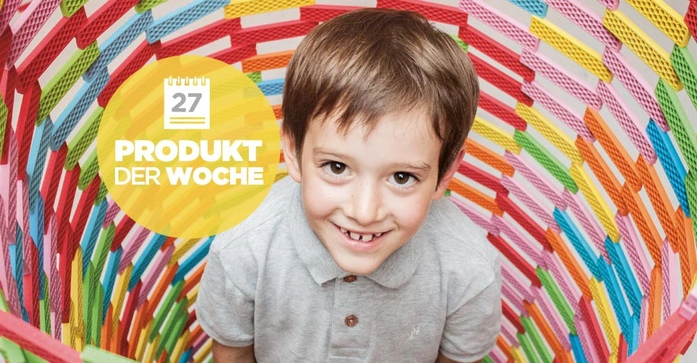 Ein lächelnder Junge, der ein graues Hemd trägt, kniet in einem bunt gewebten Korb. Der Hintergrund zeigt einen gelben Kreis mit Kalender-Icon und Text: 27 PRODUKT DER WOCHE.