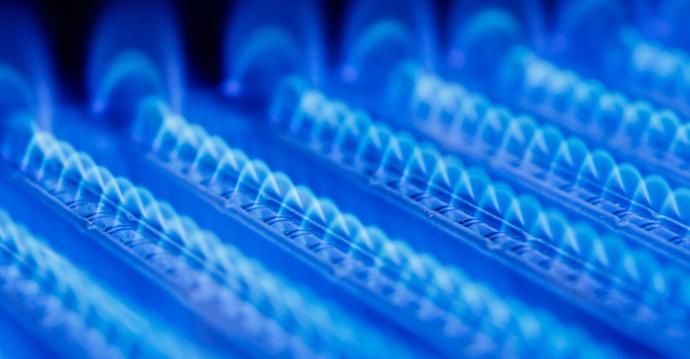 Gasflammen brennen in blauen Reihen auf einem Ofen oder Herd in einem dunklen Raum.